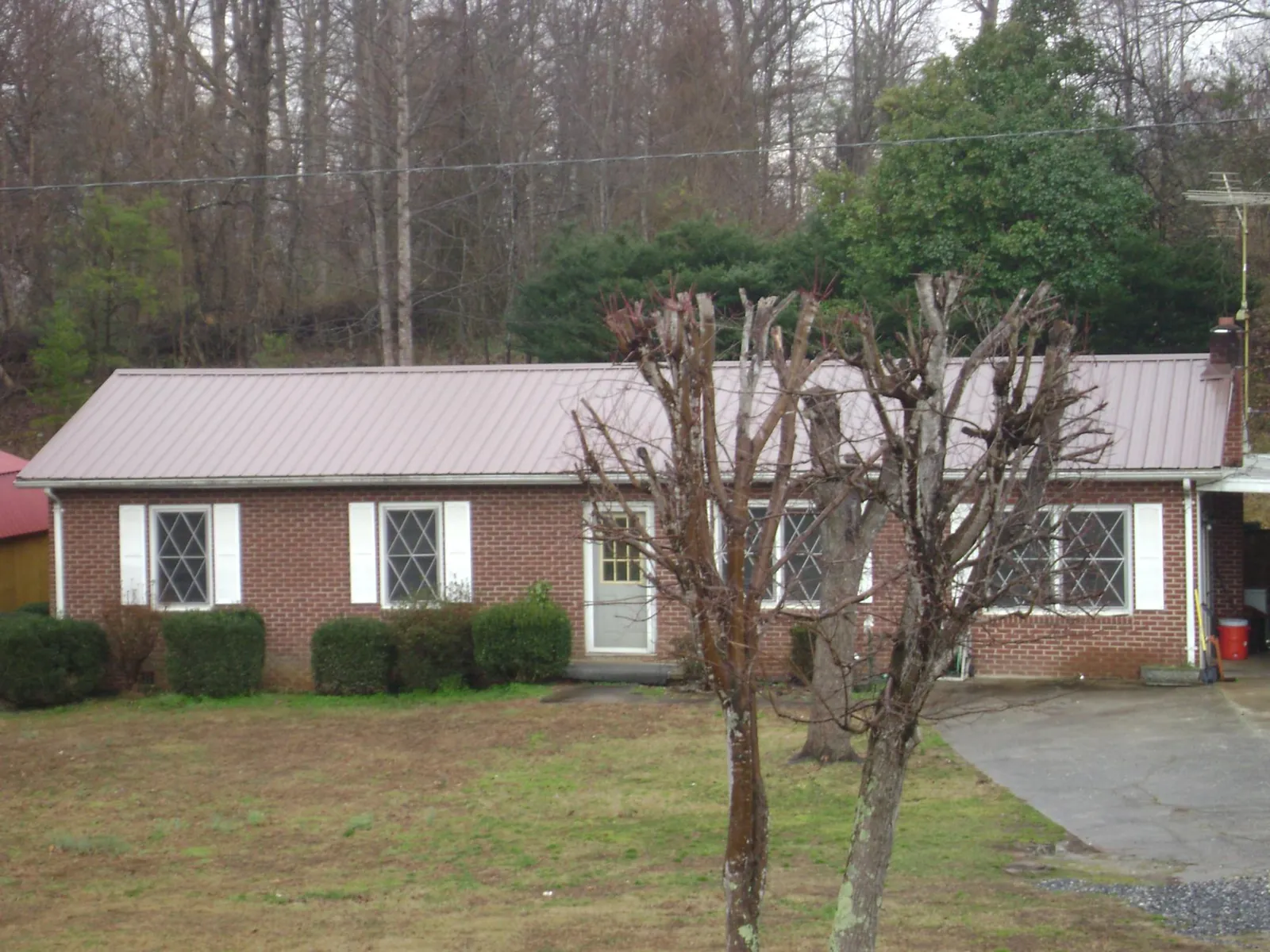 Mauve metal roof on a brick ranch home behind bare trees in Silverdale
