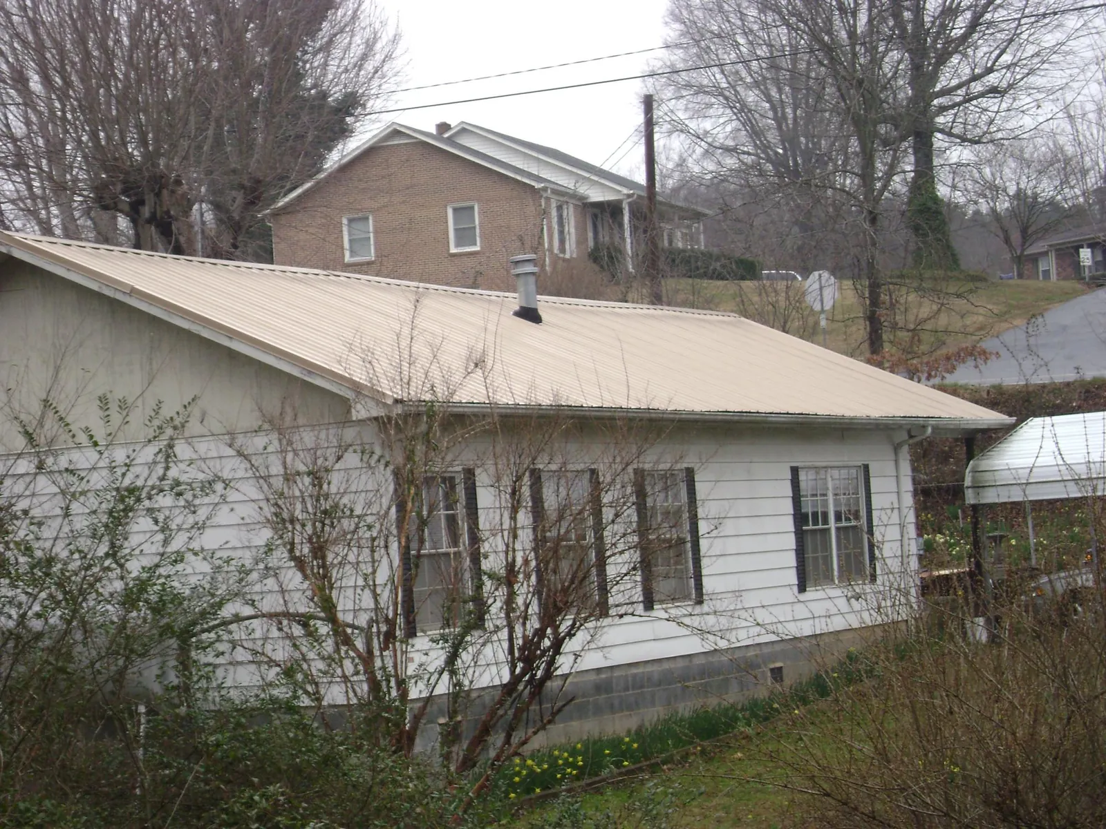 Tan metal roof on a white sided house set into a hillside — Commercial Roofing by Roofing Brothers in Silverdale